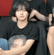 a young man in a black t-shirt is sitting on the floor with a picture of a man on his chest .
