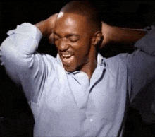 a man in a blue shirt is holding his head with his hands .