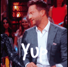 a man in a suit is sitting in front of a crowd and the word yup is written on his face