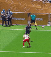 a soccer player is kicking a ball on a field with a coca cola banner behind him