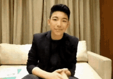 a young man is sitting on a couch with his hands folded and smiling .