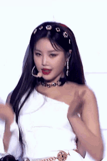 a close up of a woman wearing a white one shoulder top and a choker .