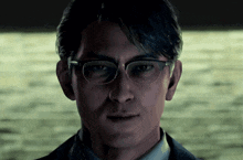a man wearing glasses looks at the camera with a serious look on his face