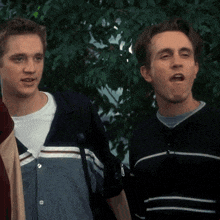 two young men standing next to each other with one wearing a striped sweater