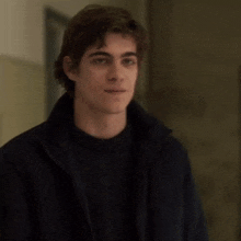 a young man wearing a black jacket and a black sweater smiles for the camera