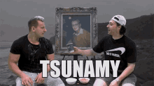 two men are sitting in front of a framed picture that says tsunami on it