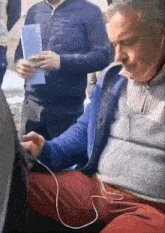 a man wearing headphones and a blue sweater is sitting in a car .
