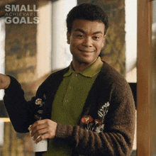 a man in a brown sweater is smiling and holding a cup of coffee