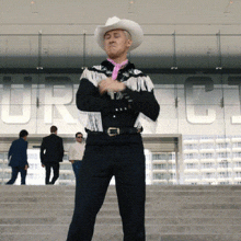 a man in a cowboy hat is standing in front of a building that has the letter c on it