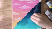 a person is painting a picture of a sunset with a bottle of acrylic paint in the background