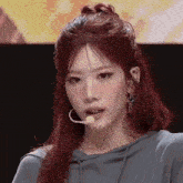 a woman with red hair is wearing a hoodie and earrings and has a microphone in her mouth .