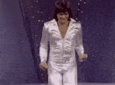 a man in a white jumpsuit is dancing on a stage in front of a blue curtain .