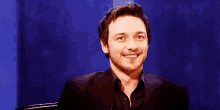 a man in a suit is sitting in front of a blue wall with the word wow on it