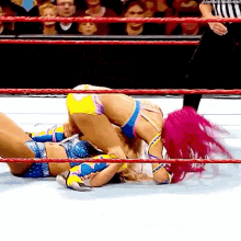 two women are wrestling in a wrestling ring while a referee watches .