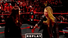 a woman in a leather jacket is standing in a wrestling ring with her hair in the air .