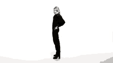 a woman in a black jumpsuit is standing in front of a white background .
