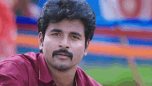 a man with a mustache wearing a red shirt looks at the camera