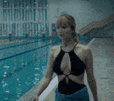 a woman in a black bathing suit is walking by a pool