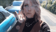a woman standing in front of a blue car with the word imgplay below her