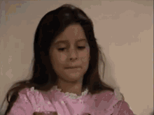 a little girl in a pink dress is making a funny face while holding a piece of cake .