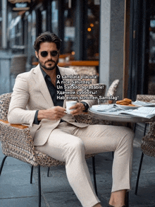 a man in a suit sits at a table with a cup of coffee in his hand