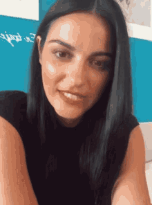 a woman with long black hair is smiling in front of a blue wall with the letter e written on it