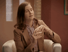 a woman in a brown jacket sits in a chair