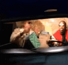 a man in a red jacket is driving a car with a woman in the back seat