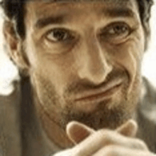 a man with a beard is making a funny face with his hands on his chin .