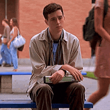 a young man sitting on a bench with a book in his hand