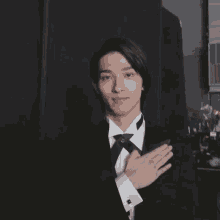a man in a tuxedo and bow tie holds his hand to his chest