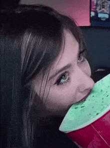 a woman is drinking from a red cup with a green leaf in her mouth .