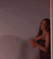 a woman in a black dress is standing in front of a wall and smiling