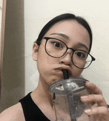 a woman wearing glasses is drinking from a clear cup
