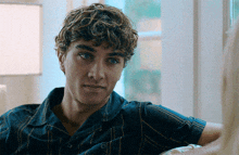 a young man with curly hair is sitting on a couch looking at the camera
