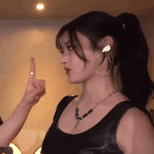 a woman wearing a black tank top and hoop earrings is pointing at someone .