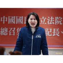 a woman wearing a blue jacket is speaking into a microphone