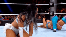two women are wrestling in a wrestling ring and one of them is laying on the floor .
