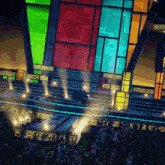 a crowd of people are gathered in front of a stage with a colorful display