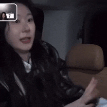 a woman is sitting in a car with her mouth open and a sign that says ' ? ' in the background