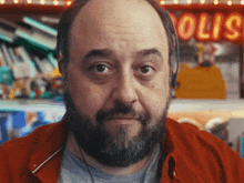 a bald man with a beard is looking at the camera in front of a sign that says " olio "
