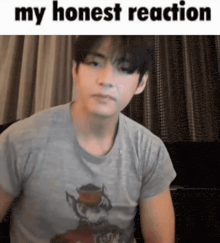 a man wearing a gray shirt is sitting on a couch and making a funny face .