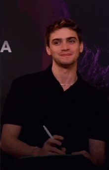 a man in a black shirt is smiling and holding a pen in front of a sign that says a