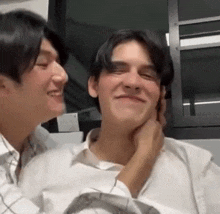 two young men are sitting next to each other and one of them is touching the other 's face .