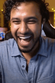 a man in a blue shirt is laughing with his mouth wide open