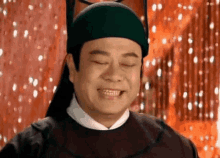 a man wearing a green hat and a black robe is smiling .