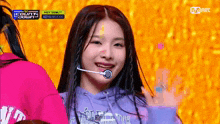 a young girl wearing a purple hoodie and a microphone is smiling on a stage .