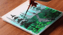 a person is painting a landscape with a brush on a piece of paper