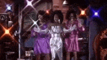 a group of women in purple dresses are dancing on a stage .