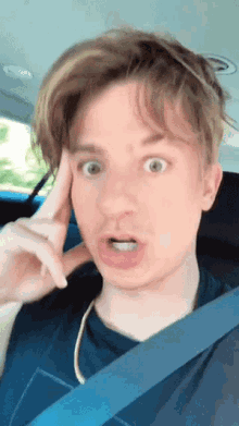 a young man wearing a blue shirt and a blue seat belt makes a surprised face